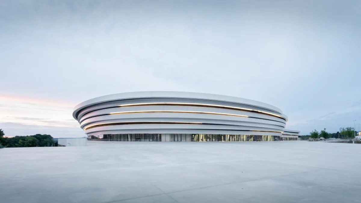 Vue au sol du parvis vierge devant l'Arena : grande esplanade en béton, surface disponible pour les stands